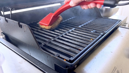 Personne qui nettoie un barbecue avec une brosse