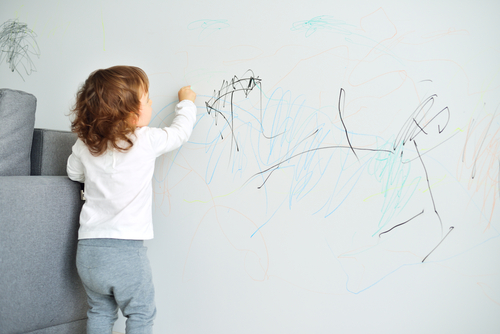 Nettoyer les traces de crayon sur un mur Jeune enfant qui gribouille sur un mur